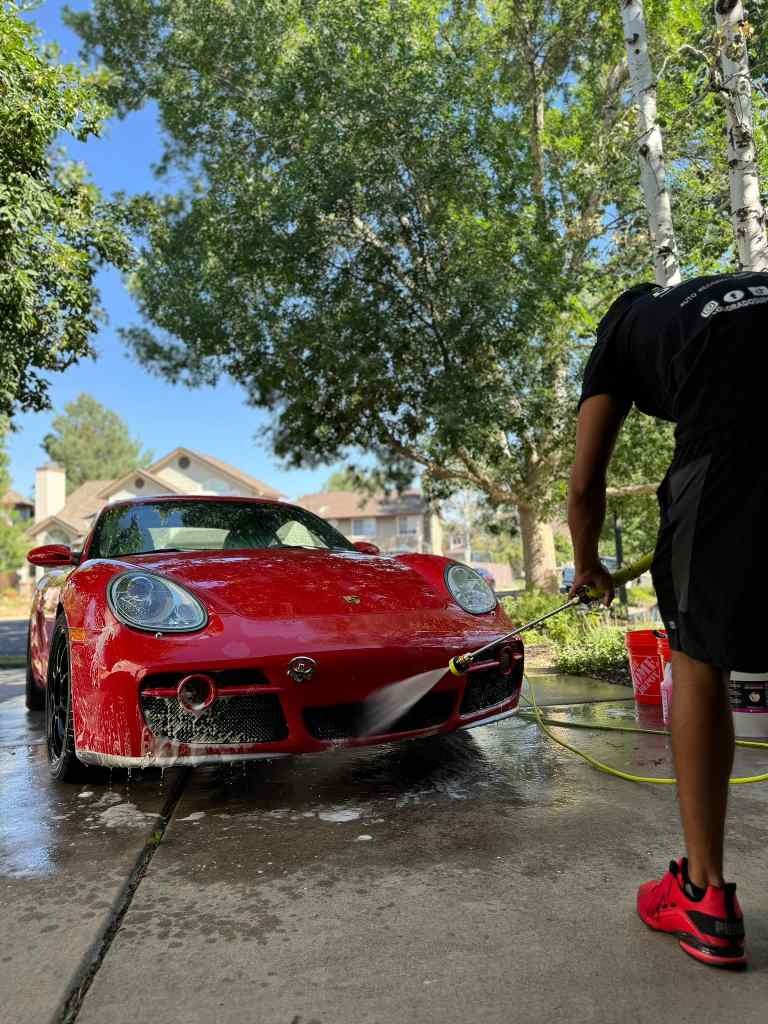 Expert technician rinsing the vehicle as part of the best detailing service, ensuring a thorough clean before the next steps in the professional detailing process, delivering a flawless finish with top-tier care and attention to detail